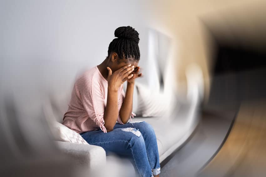 woman holding her head in pain on couch