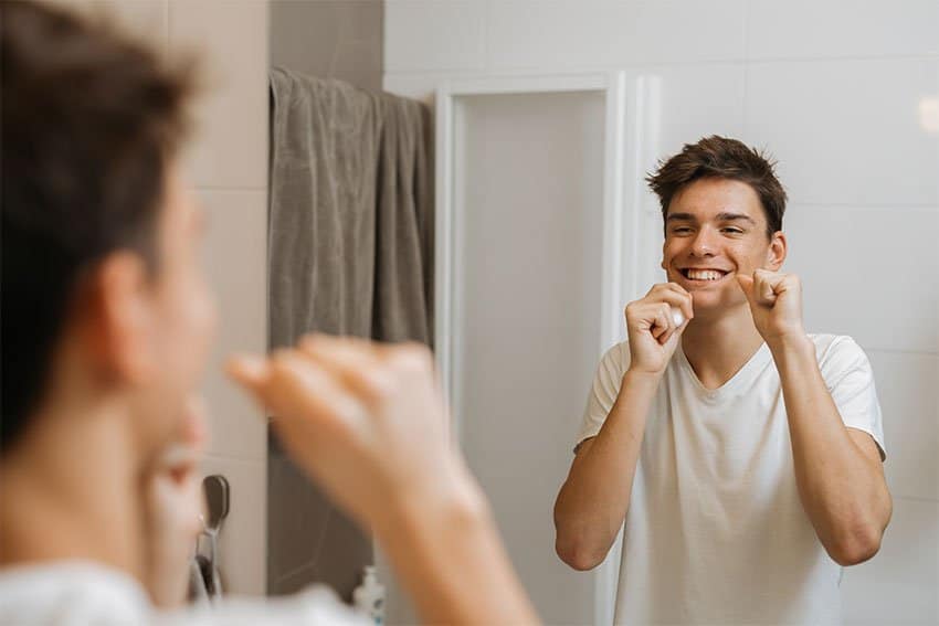 young man flossing his teeth in front of mirror in bathroom