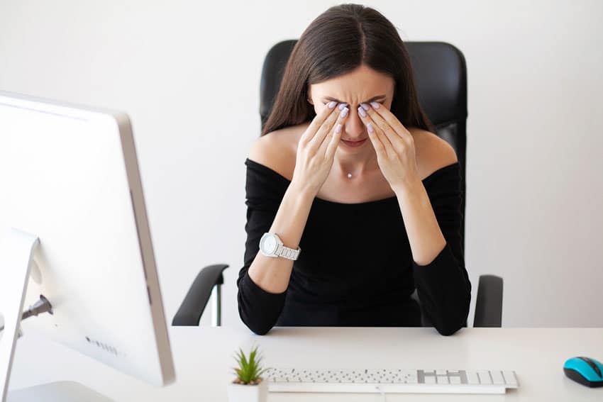 fatigued woman rubbing eyes at work desk